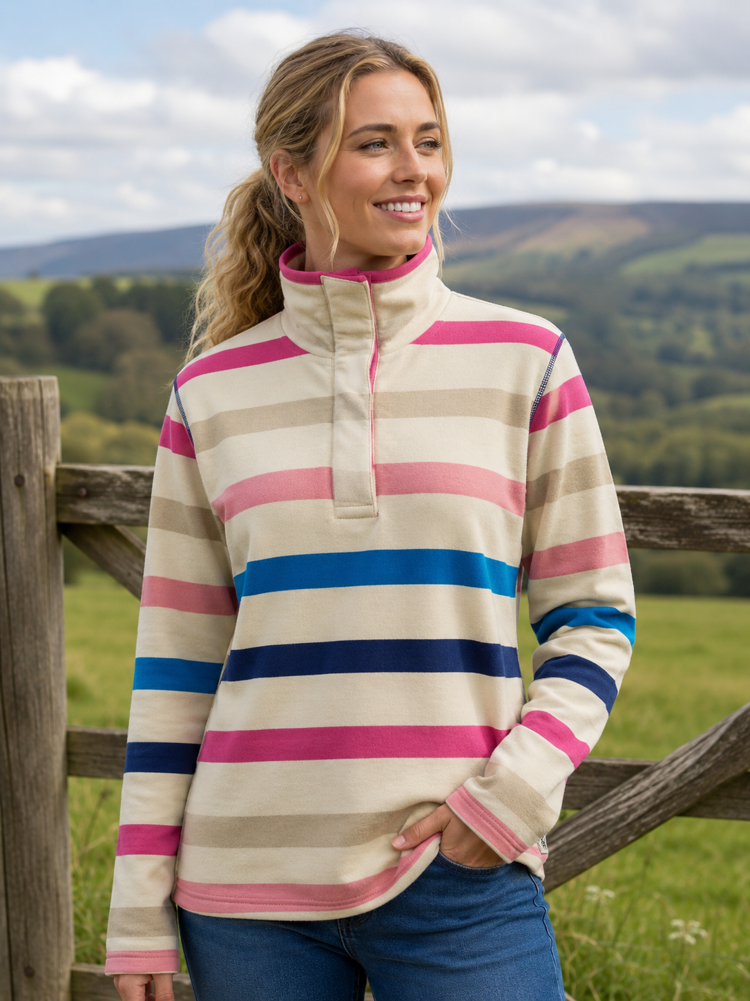 Woman wearing a striped sweater standing in a field with mountains in the background