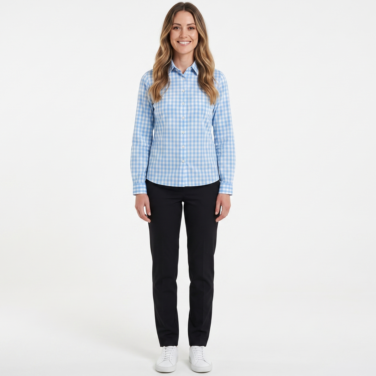 A woman modeling a light blue and white gingham long-sleeve button-down shirt, paired with black pants and white sneakers, against a plain white studio background.