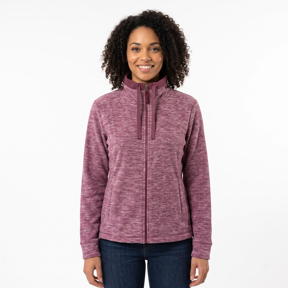 A woman with curly dark hair wearing a heathered mauve-purple full-zip fleece jacket and dark blue jeans, standing against a plain white studio background.