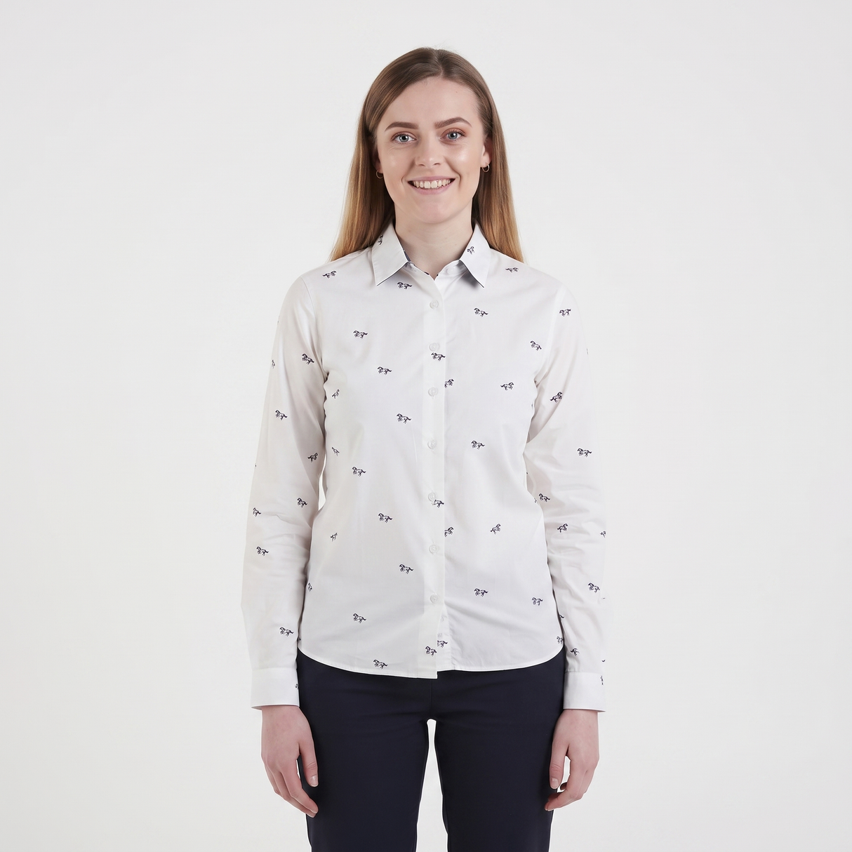 A woman modeling a white long-sleeve button-up shirt with a small black bow pattern, paired with dark navy pants, against a plain white studio background.
