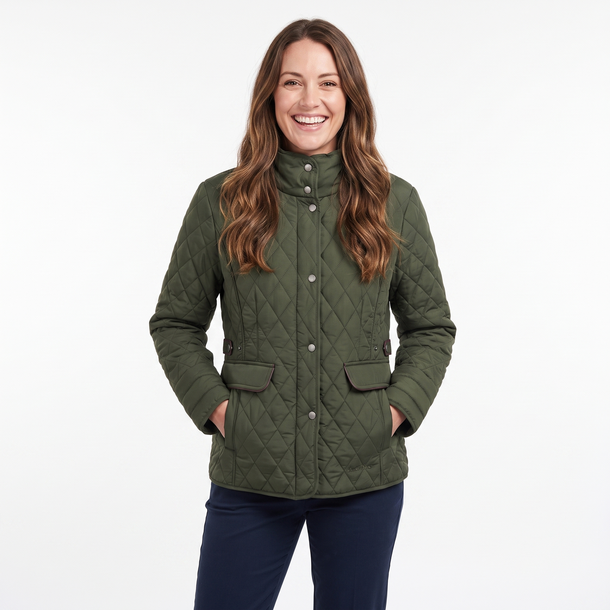 A smiling woman with long brown hair models an olive green diamond-quilted jacket with a high collar and front buttons, paired with navy blue pants, against a plain white studio background.