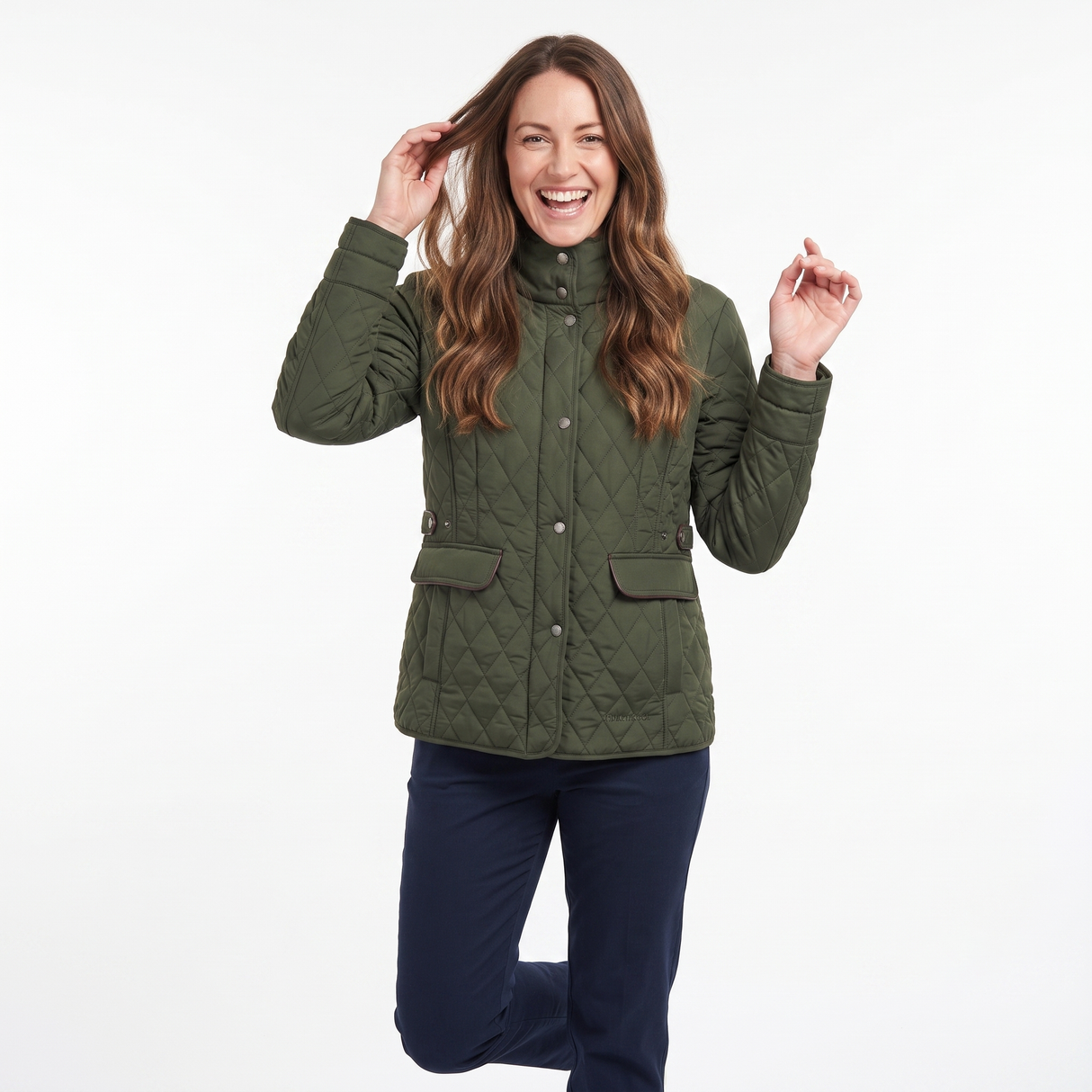 A woman smiling and posing in a quilted olive green jacket with dark navy pants, set against a plain white studio background.