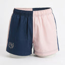 A pair of split-color shorts with one side in navy blue and the other in light pink, featuring a white embroidered monogram logo on the navy side and piping details, displayed on a white mannequin against a white background.
