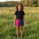 Child wearing a black shirt and colorful shorts standing in a grassy field.