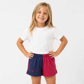 Young girl wearing a white t-shirt and red and blue shorts on a white background