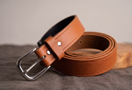 Brown leather belt with silver buckle on a textured surface