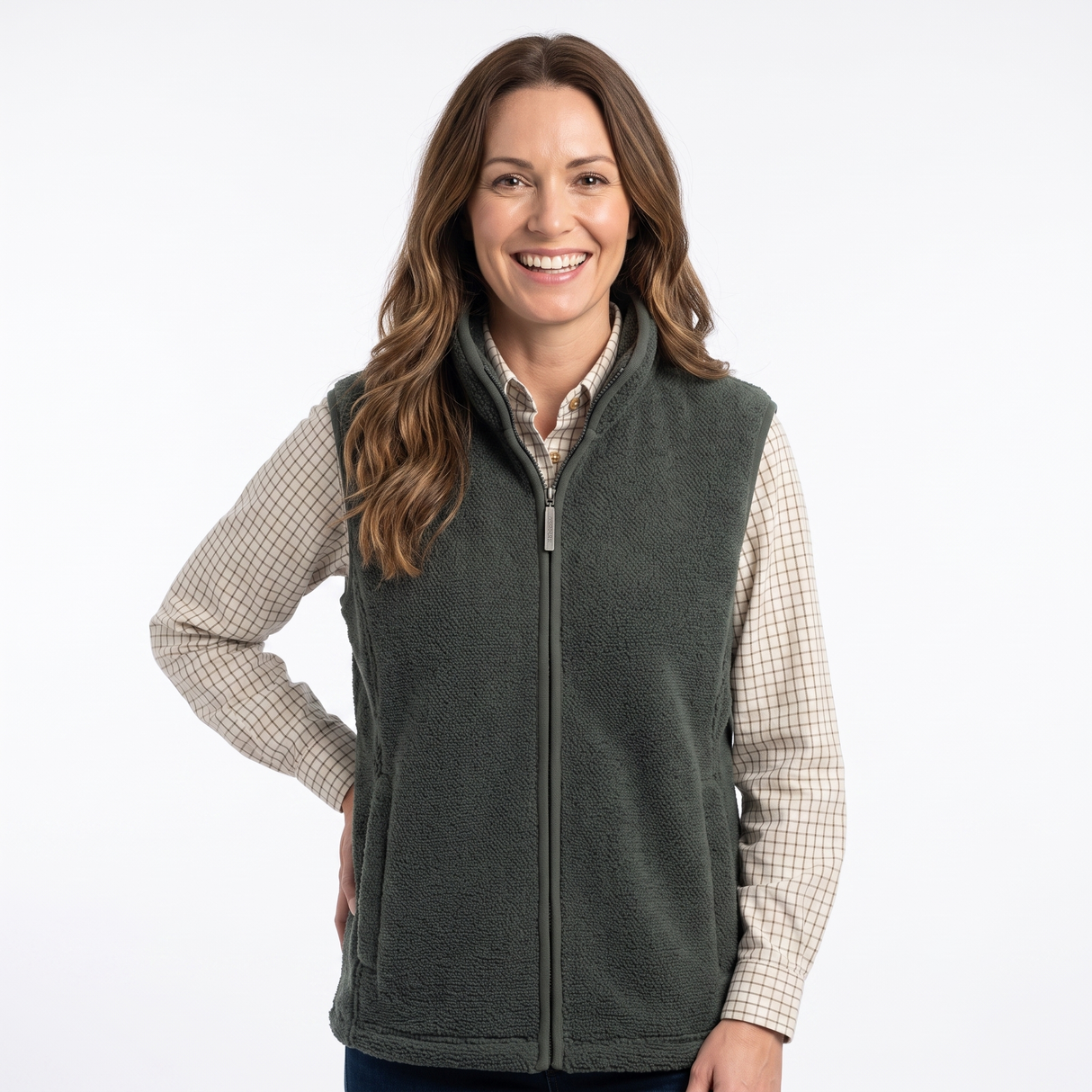 A smiling woman wearing a dark olive green zip-up fleece vest over a beige and white checkered long-sleeve shirt, photographed against a clean white studio background.