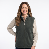 A smiling woman wearing a dark olive green zip-up fleece vest over a beige and white checkered long-sleeve shirt, photographed against a clean white studio background.