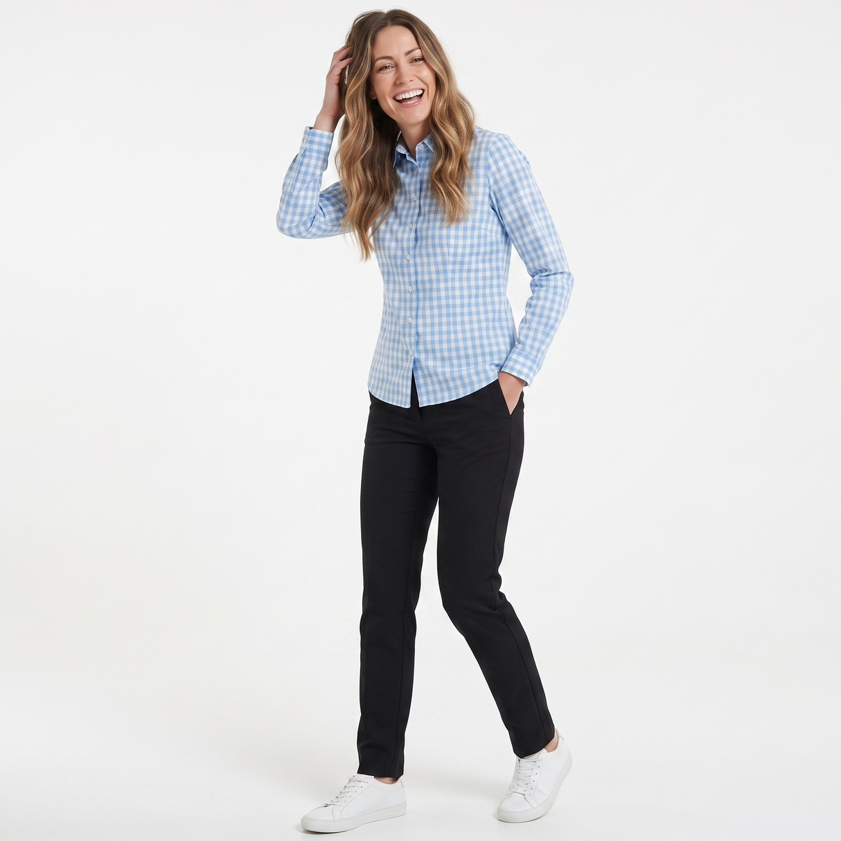 A woman modeling a light blue and white gingham long-sleeve button-down shirt, paired with black pants and white sneakers, against a plain white studio background.