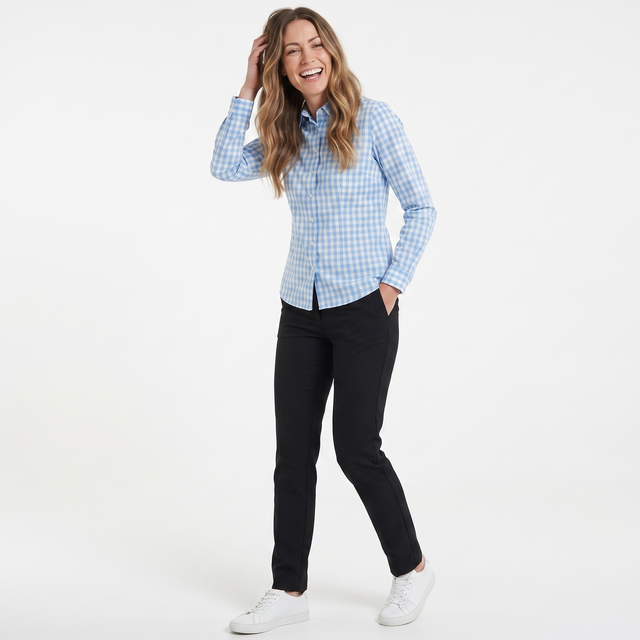A woman modeling a light blue and white gingham long-sleeve button-down shirt, paired with black pants and white sneakers, against a plain white studio background.