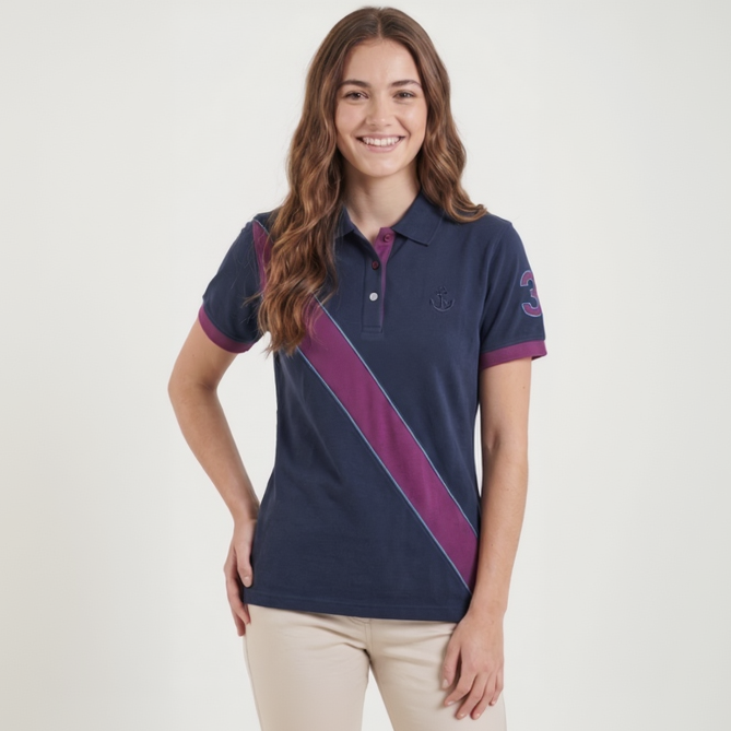 A woman modeling a navy blue short-sleeve polo shirt with a diagonal magenta stripe and a small embroidered logo on the chest, paired with beige pants, against a plain white studio background.