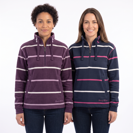 Two women modeling striped quarter-zip hooded sweatshirts against a plain white studio background. The woman on the left wears a plum purple hoodie with white and light pink horizontal stripes, and the woman on the right wears a navy blue hoodie with white and pink horizontal stripes.