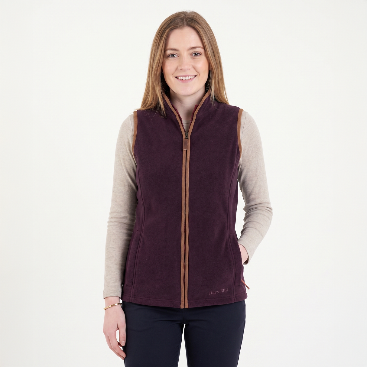 Woman wearing a purple vest over a beige long-sleeve shirt on a white background