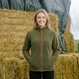Woman in a green jacket standing in front of hay bales