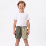 A young boy standing against a white studio background, wearing a white short-sleeve t-shirt and split-color shorts with one leg in olive green and the other in light khaki.