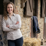 Woman standing in front of a stable with hay bales and a red bucket.
